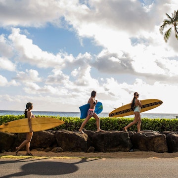 Pacific Islander surfers carry their boards to the water.